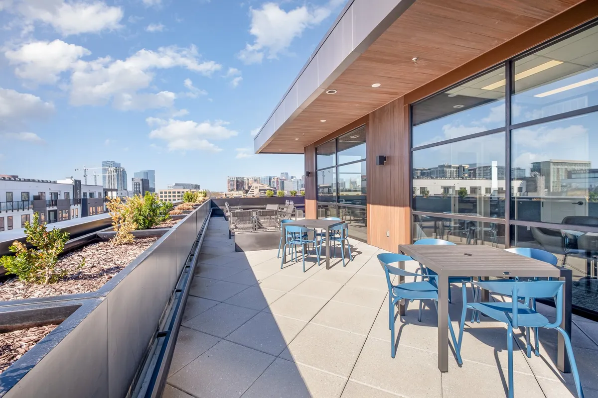 A stylish rooftop lounge with modern outdoor seating, planters with greenery, and a panoramic city skyline view. The atmosphere is perfect for sunset gatherings or casual weekend brunches.