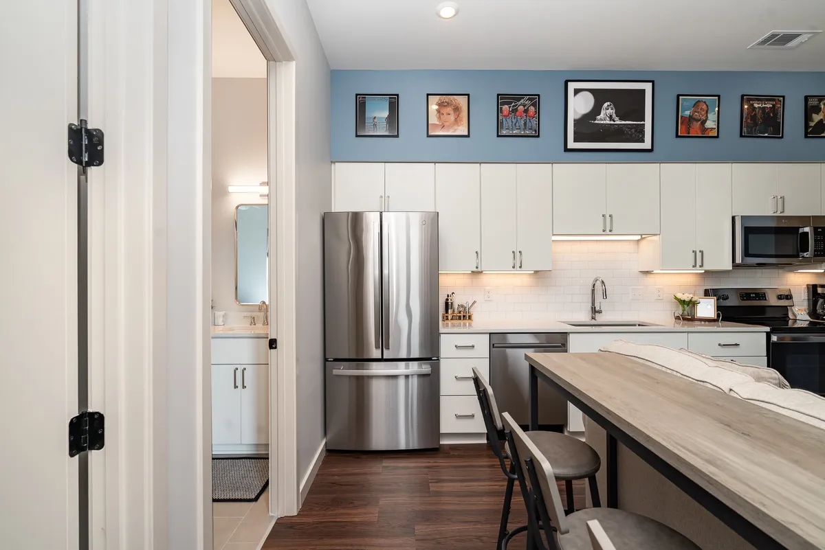 A view of a modern, cozy kitchen featuring a kitchen island, stainless steel appliances, framed artwork, and an open layout that encourages socializing. The space is sunlit, with inviting touches that make it ideal for gathering and meal preparation.