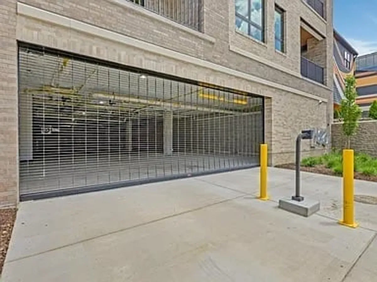 A secure garage entrance featuring a security grille and yellow bollards. The image conveys ease of access and a practical, protected environment for vehicles.