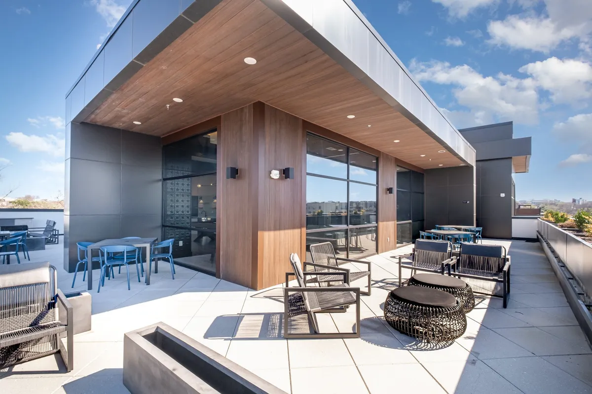 This rooftop lounge scene features stylish outdoor furniture, glass railings, and a warm wooden ceiling. The setting boasts stunning city views and a relaxed ambiance, suggesting a perfect spot for unwinding after work or a medical visit.