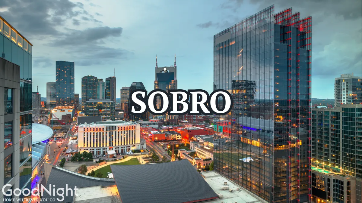 A dynamic city view at sunset, featuring the illuminated Nashville skyline and the SOBRO sign. The image conveys the allure of nightlife and city exploration, with the glow of buildings suggesting energy and excitement.