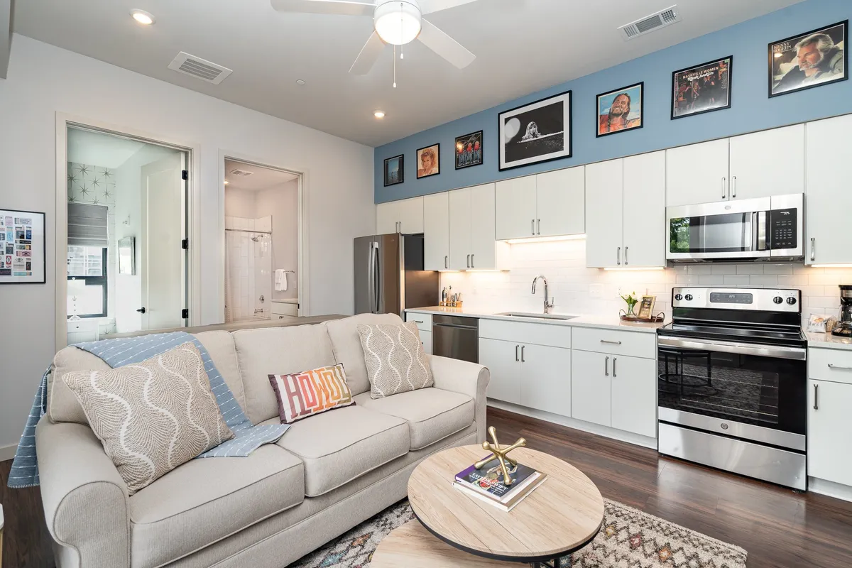 The image showcases a stylish, open-concept living area with a comfortable sofa, modern kitchen cabinetry, vibrant artwork on the wall, and a chic coffee table. The space is designed for both relaxation and entertaining, featuring tasteful decor and inviting ambiance.