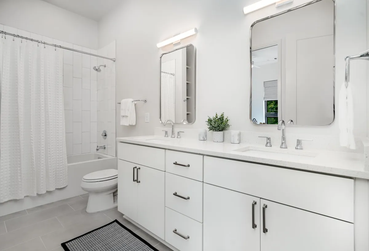 A modern Jack-n-Jill bathroom featuring double sinks, large mirrors, a stylish shower area, and well-organized amenities, all in a refreshing, bright setting.