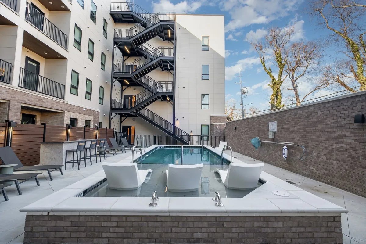 A contemporary outdoor swimming pool area surrounded by modern lounge chairs and an exterior staircase. The pool is inviting, with clean lines and stylish furniture, ideal for relaxation and socializing on sunny days.