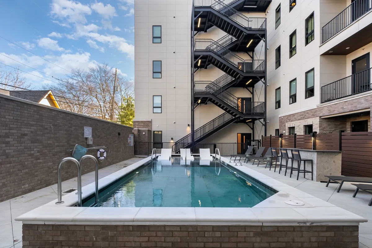 A sparkling swimming pool is surrounded by outdoor seating and is adjacent to the building facade. The scene radiates relaxation and the social atmosphere of summer days, with the pool area inviting for both children and adults.